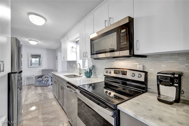 kitchen with light stone counters, stainless steel appliances, backsplash, white cabinets, and a sink