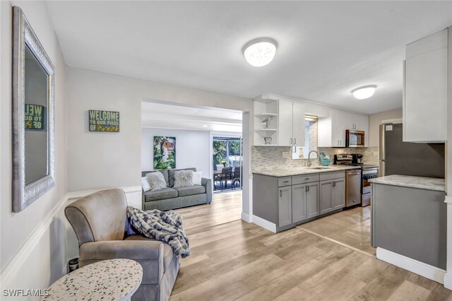 kitchen with decorative backsplash, appliances with stainless steel finishes, light wood-type flooring, sink, and gray cabinets