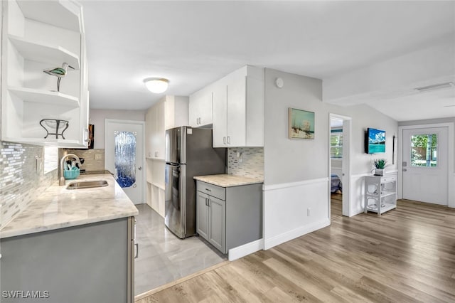 kitchen featuring open shelves, gray cabinetry, freestanding refrigerator, a healthy amount of sunlight, and a sink