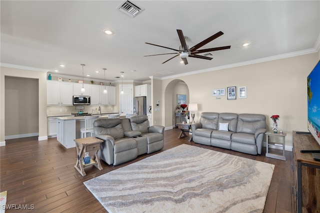 living room with ceiling fan, sink, ornamental molding, and dark wood-type flooring