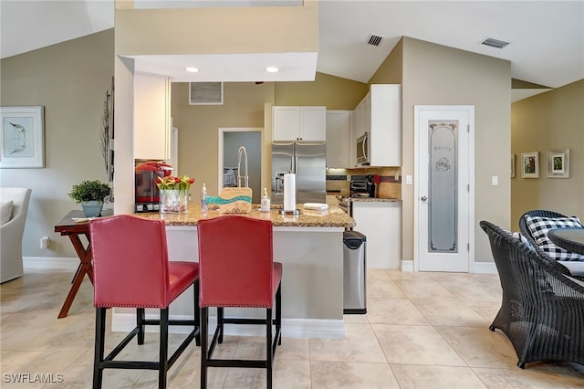 kitchen featuring a kitchen bar, appliances with stainless steel finishes, light stone counters, white cabinets, and lofted ceiling