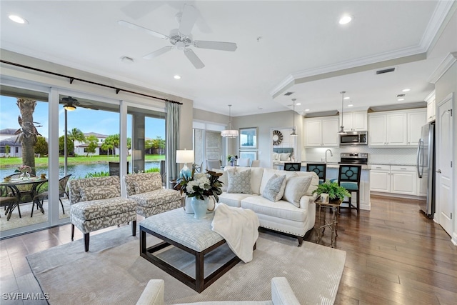 living room featuring a water view, dark hardwood / wood-style floors, ornamental molding, and ceiling fan