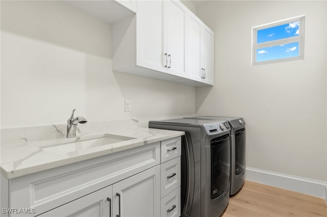 laundry room with cabinets, light wood-type flooring, washing machine and dryer, and sink