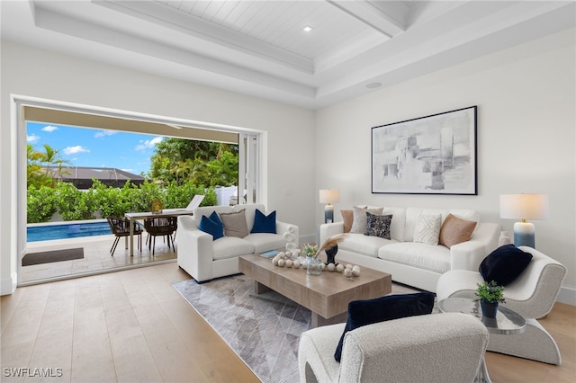 living room with beam ceiling, a raised ceiling, and light hardwood / wood-style floors