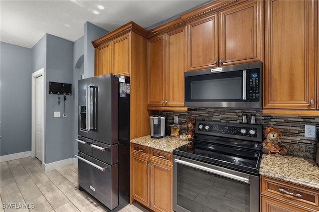 kitchen featuring light stone counters, light wood-type flooring, appliances with stainless steel finishes, and tasteful backsplash