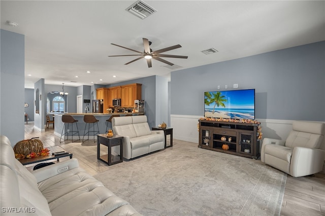 living room with ceiling fan with notable chandelier and light wood-type flooring