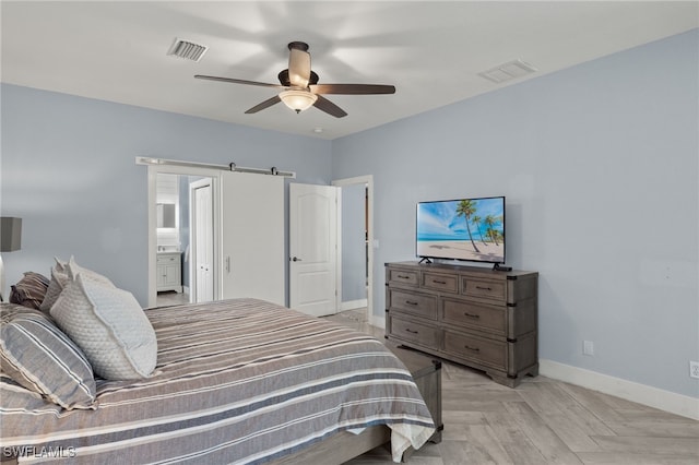 bedroom featuring a barn door, ceiling fan, light parquet flooring, and connected bathroom