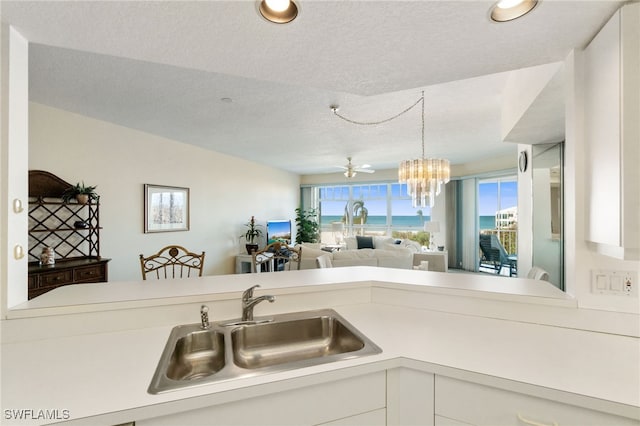 kitchen featuring ceiling fan with notable chandelier, sink, hanging light fixtures, a textured ceiling, and white cabinetry