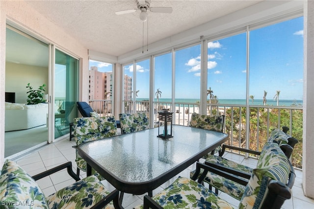 sunroom / solarium featuring ceiling fan, a water view, and a beach view