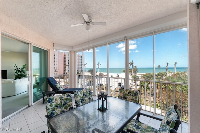 sunroom / solarium featuring ceiling fan, a water view, and a view of the beach