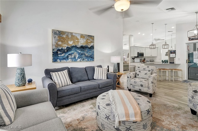 living room featuring ceiling fan with notable chandelier and light hardwood / wood-style flooring