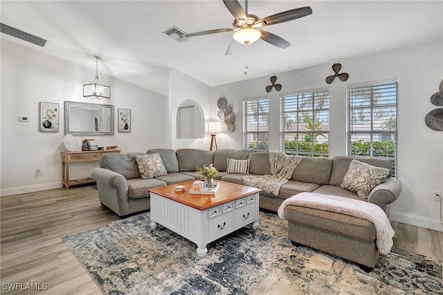 living room featuring ceiling fan with notable chandelier, vaulted ceiling, and light wood-type flooring