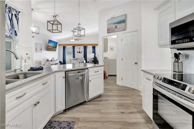 kitchen featuring pendant lighting, sink, light wood-type flooring, white cabinetry, and stainless steel appliances