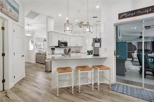 kitchen with kitchen peninsula, light wood-type flooring, tasteful backsplash, ceiling fan, and white cabinetry