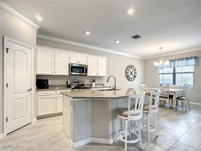 kitchen with light stone counters, stainless steel appliances, sink, white cabinetry, and an island with sink