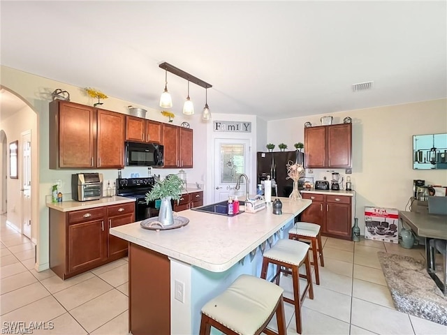 kitchen featuring pendant lighting, a kitchen island with sink, black appliances, a kitchen breakfast bar, and light tile patterned flooring