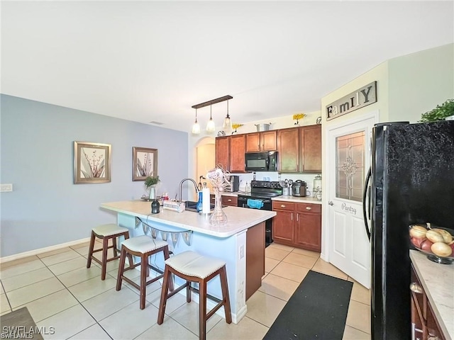 kitchen with hanging light fixtures, a breakfast bar, light tile patterned flooring, black appliances, and a center island with sink