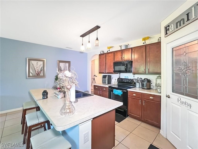 kitchen with a kitchen breakfast bar, black appliances, pendant lighting, light tile patterned floors, and an island with sink