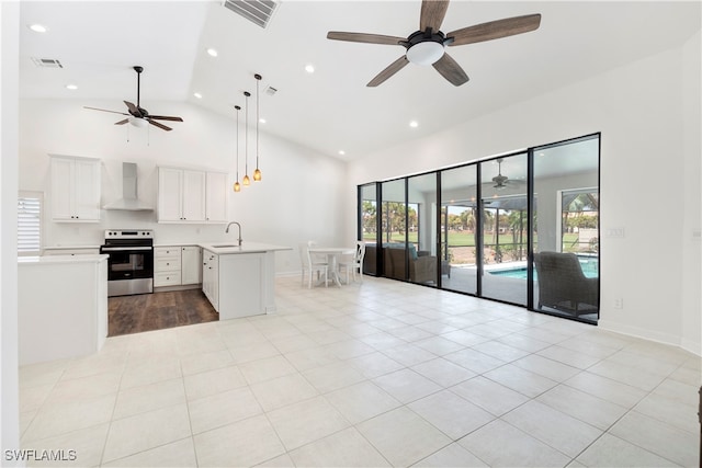 kitchen featuring a wealth of natural light, stainless steel electric range oven, white cabinets, and wall chimney range hood