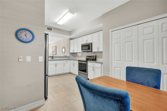 kitchen featuring white cabinets, decorative backsplash, light tile patterned flooring, and appliances with stainless steel finishes