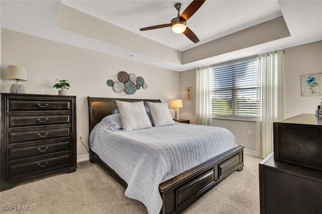 bedroom featuring a raised ceiling, ceiling fan, and light colored carpet