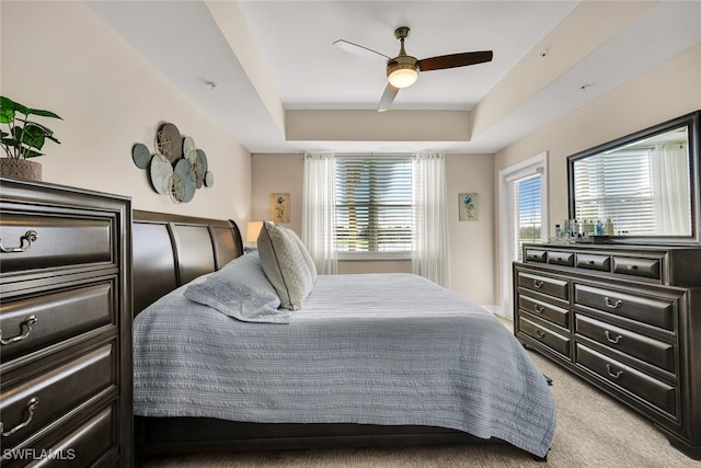 carpeted bedroom featuring a tray ceiling and ceiling fan