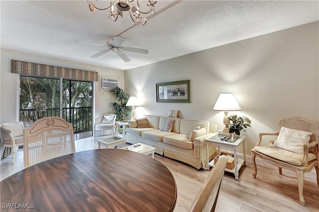 living room with ceiling fan with notable chandelier, a textured ceiling, a wall unit AC, and light hardwood / wood-style flooring