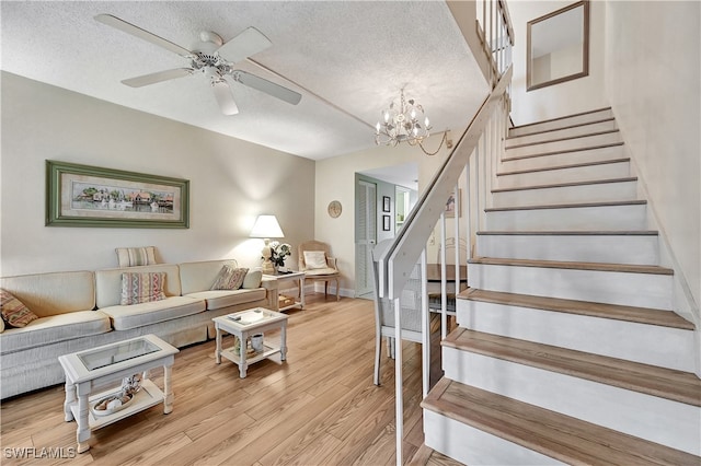 living room with ceiling fan with notable chandelier, light wood-type flooring, and a textured ceiling