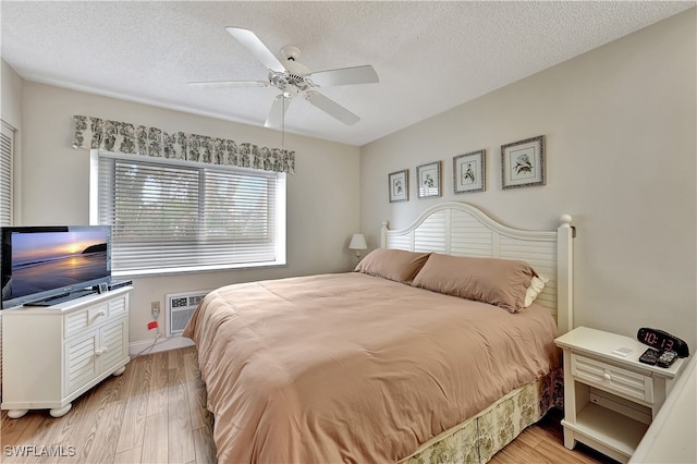 bedroom with a wall mounted AC, a textured ceiling, light wood-type flooring, and ceiling fan