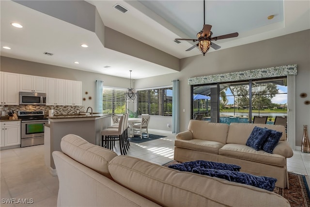 living room with ceiling fan with notable chandelier, a wealth of natural light, and light tile patterned flooring