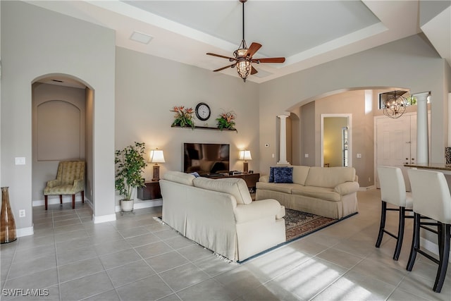 living room featuring light tile patterned floors, ceiling fan with notable chandelier, decorative columns, and a high ceiling