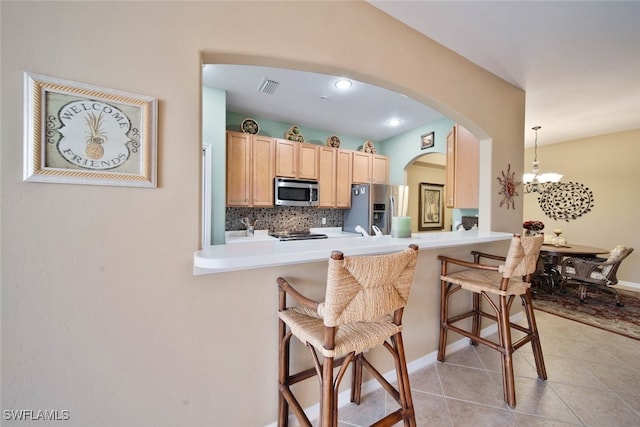 kitchen with appliances with stainless steel finishes, light brown cabinetry, a breakfast bar, pendant lighting, and an inviting chandelier