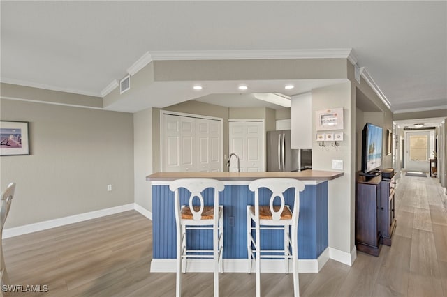 kitchen featuring stainless steel refrigerator, kitchen peninsula, light hardwood / wood-style floors, a kitchen bar, and ornamental molding