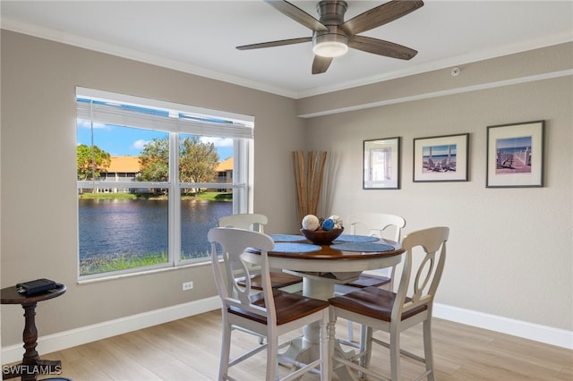 dining space with ceiling fan, crown molding, a water view, and light wood-type flooring