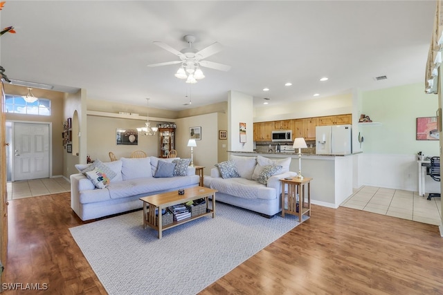 living room with light hardwood / wood-style floors and ceiling fan with notable chandelier