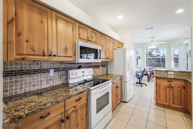 kitchen featuring ceiling fan, backsplash, dark stone counters, white appliances, and light tile patterned floors