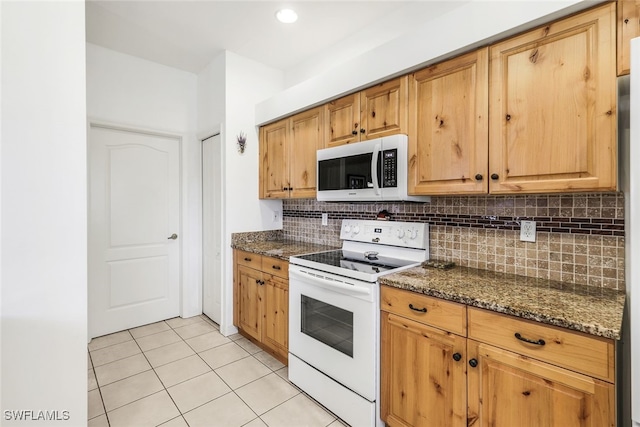 kitchen featuring tasteful backsplash, dark stone countertops, light tile patterned floors, and white appliances