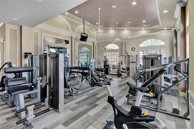 gym featuring light wood-type flooring, ornamental molding, and a high ceiling