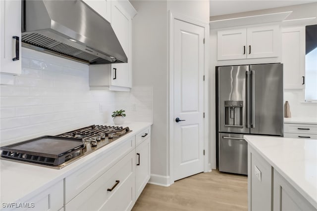 kitchen with white cabinets, light wood-type flooring, stainless steel appliances, and exhaust hood