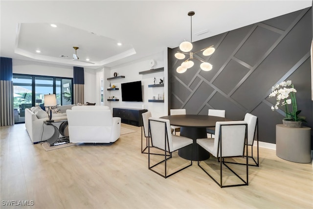 dining space with a notable chandelier, light hardwood / wood-style floors, and a tray ceiling