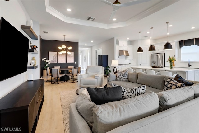 living room with a chandelier, ornamental molding, a tray ceiling, and light hardwood / wood-style flooring