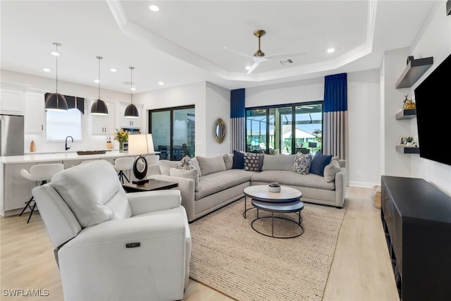 living room with light wood-type flooring, a tray ceiling, and ceiling fan