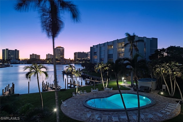 pool at dusk featuring a water view and a patio