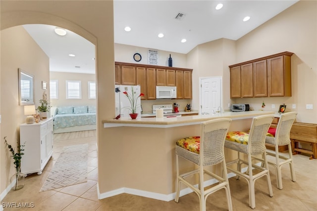 kitchen with a breakfast bar area, kitchen peninsula, light tile patterned flooring, and white appliances