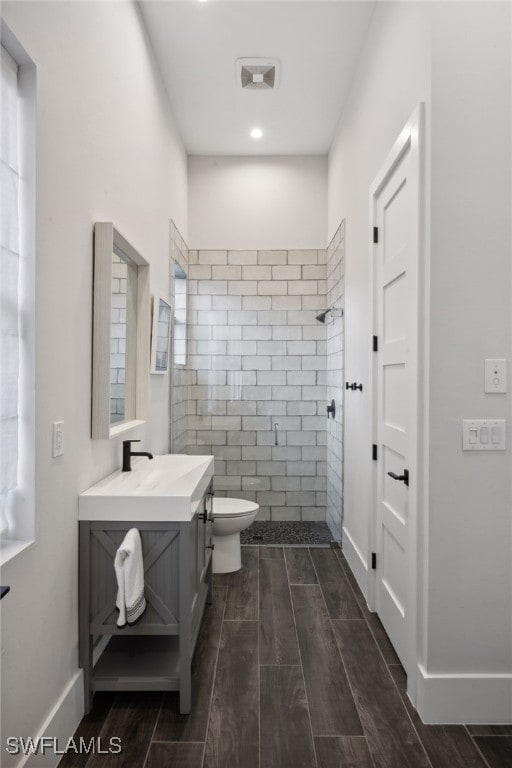 bathroom featuring vanity, toilet, a tile shower, and a wealth of natural light