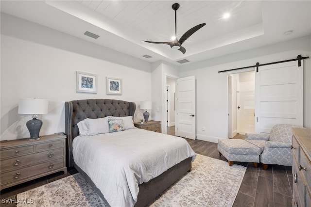 bedroom featuring ensuite bath, ceiling fan, dark wood-type flooring, a raised ceiling, and a barn door