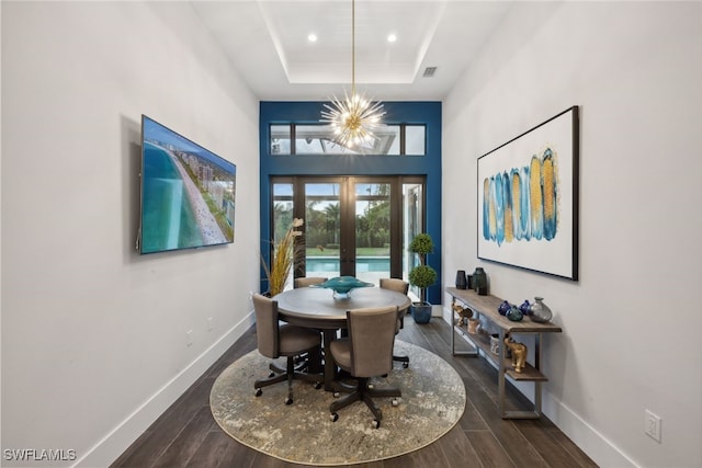 dining space featuring french doors, an inviting chandelier, a raised ceiling, dark hardwood / wood-style floors, and a towering ceiling