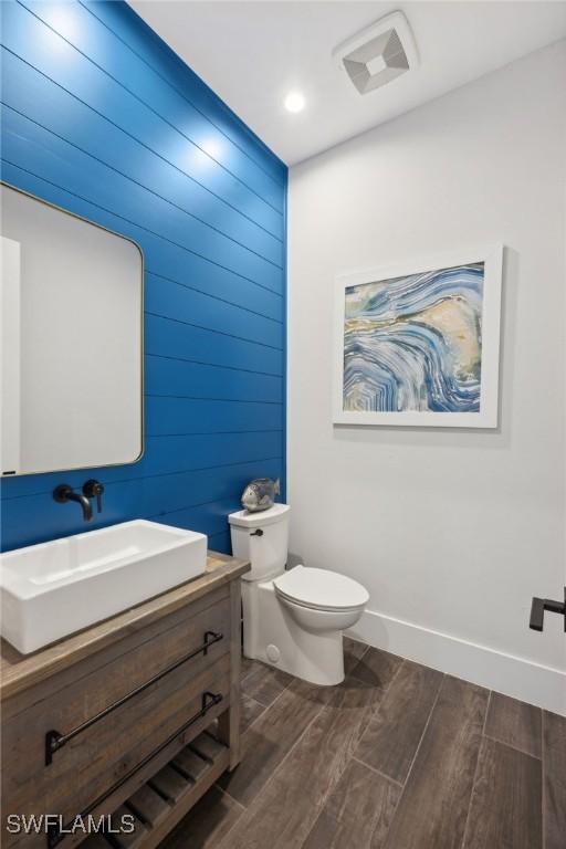 bathroom with vanity, wood walls, toilet, and wood-type flooring