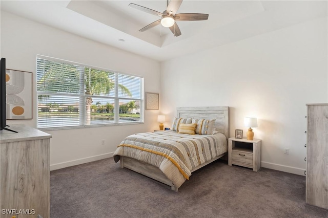 carpeted bedroom with a tray ceiling, baseboards, and ceiling fan