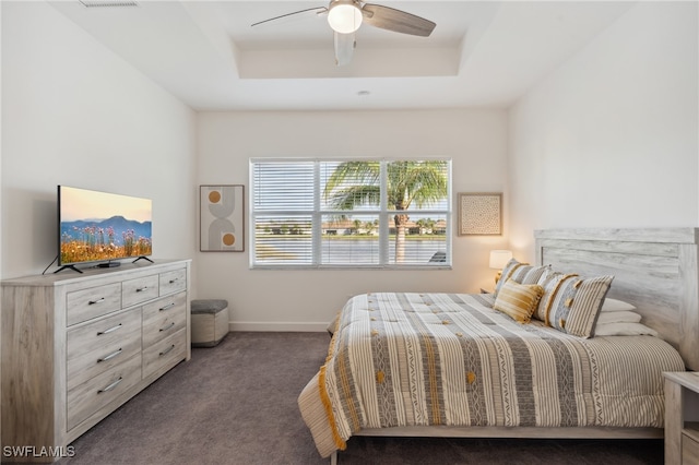 bedroom with a raised ceiling, ceiling fan, and dark colored carpet